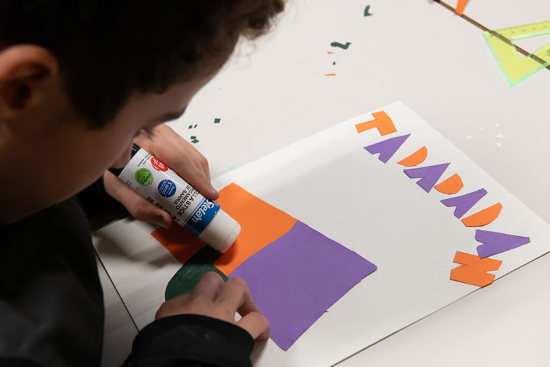 Ragazzo incolla lettere di carta colorata su un cartoncino