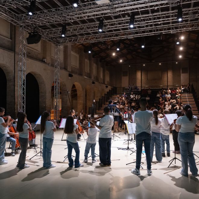 Giovani musicisti suonano strumenti ad arco in un grande ex spazio industriale davanti al pubblico