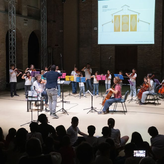 Orchestra di bambini in concerto davanti al pubblico, con una proiezione sullo sfondo
