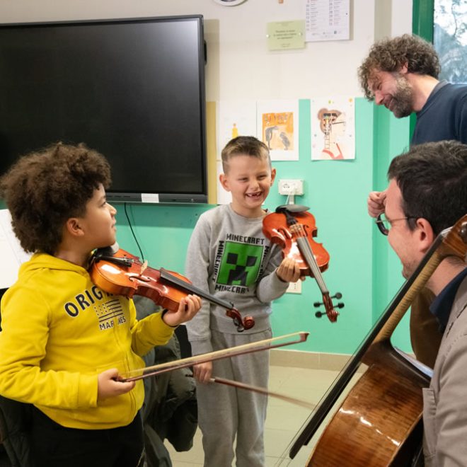 Due musicisti insegnano a due bambini a suonare il violino in classe