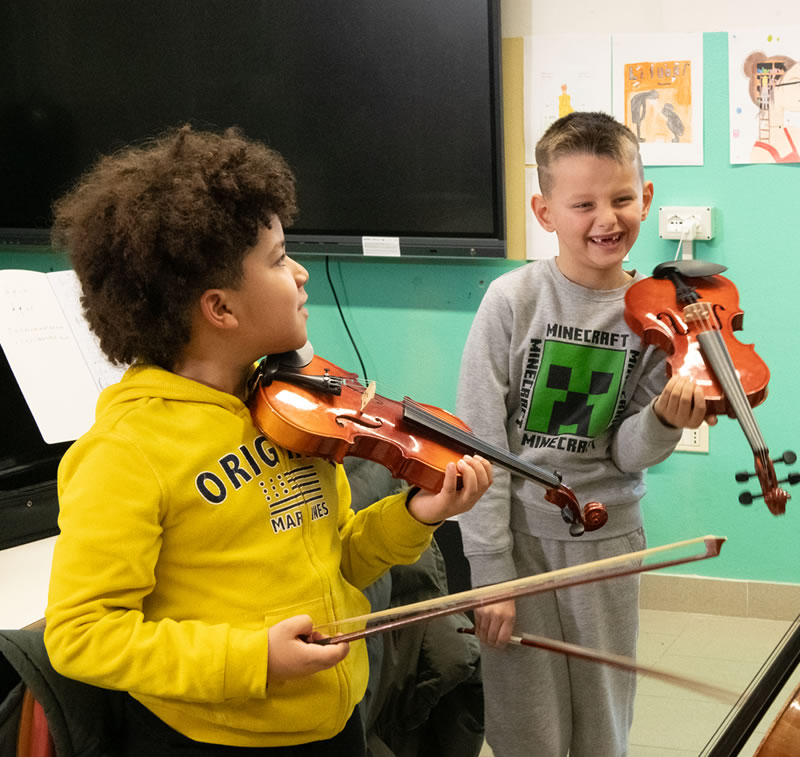 Due bambini sorridenti suonano il violino in classe